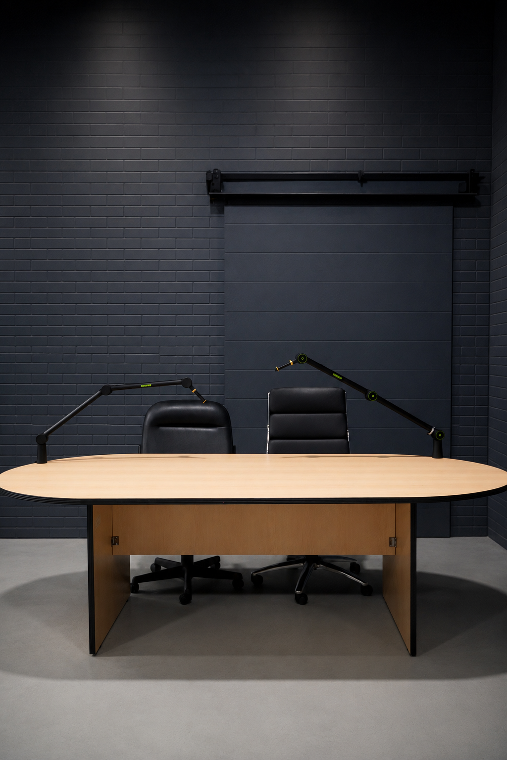 Podcast setup with two mic booms, chairs and a wood table against a dark brick wall